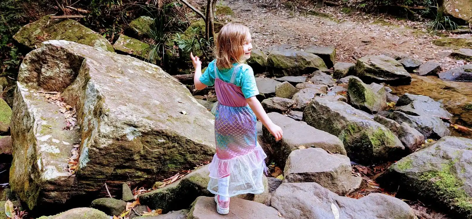 kid crossing a river on a hike in a mermaid outfit